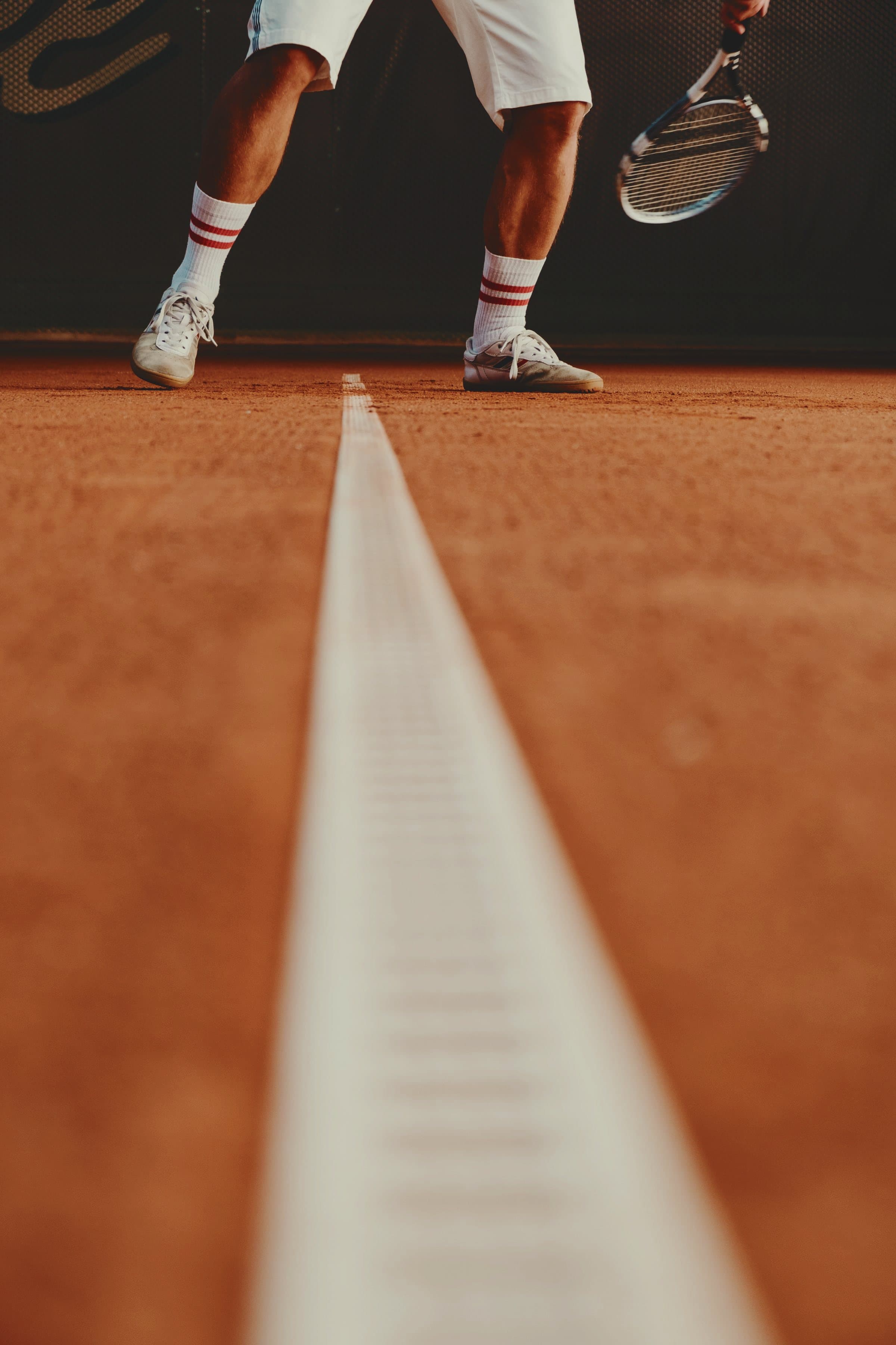 A player’s feet on a red clay court beside the baseline